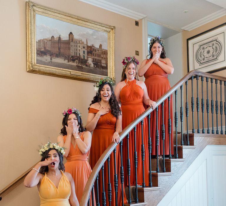 Bridesmaids stand on staircase wearing ombre styled bridesmaid dresses in yellow and orange 