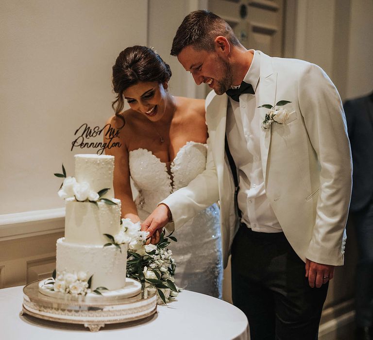 The bride and groom cut their three tier frosted wedding cake with a personalised cake topper 