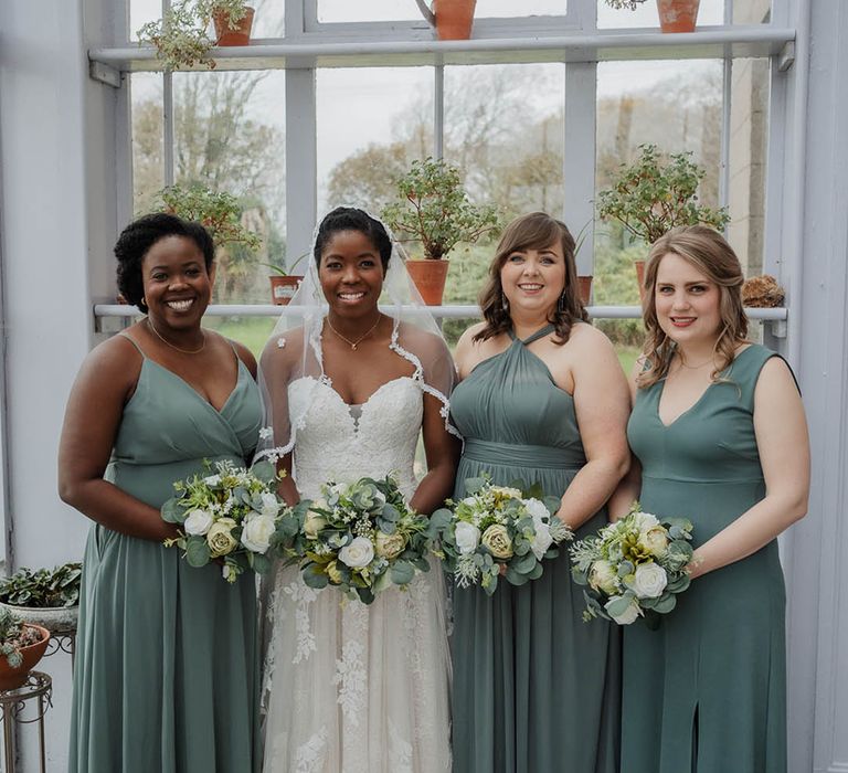 Bridesmaids in green dresses in a variety of styles with the bride in a strapless lace wedding dress 