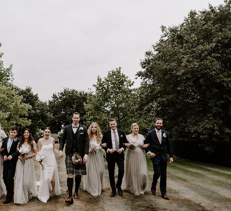 The bridesmaids wear matching sequin sparkly dresses with the groomsmen in suits and kilts walking with he bride and groom on the wedding day 