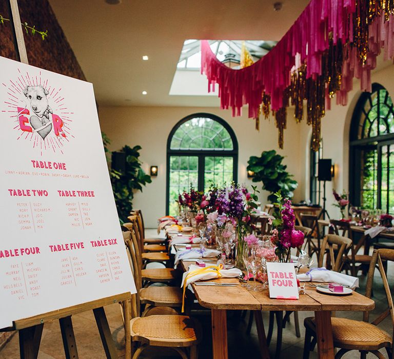 Retro light pink wedding table plan with hot pink writing standing on wooden easel beside an exposed brick wall in the Middleton Lodge reception room