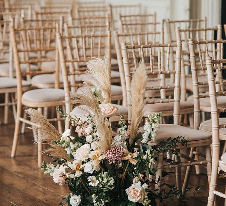 Rose, pampas grass and bell flowers in pink and white neutral shades decorate the aisle for wedding at Elmore Court 