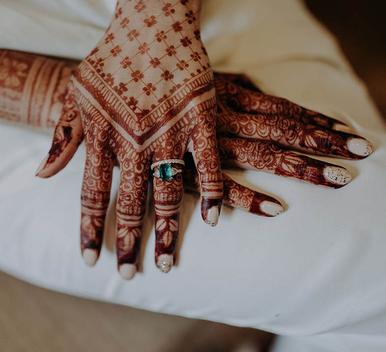 Bride wears white and sparkling nail polish and intricate henna design across her hands 