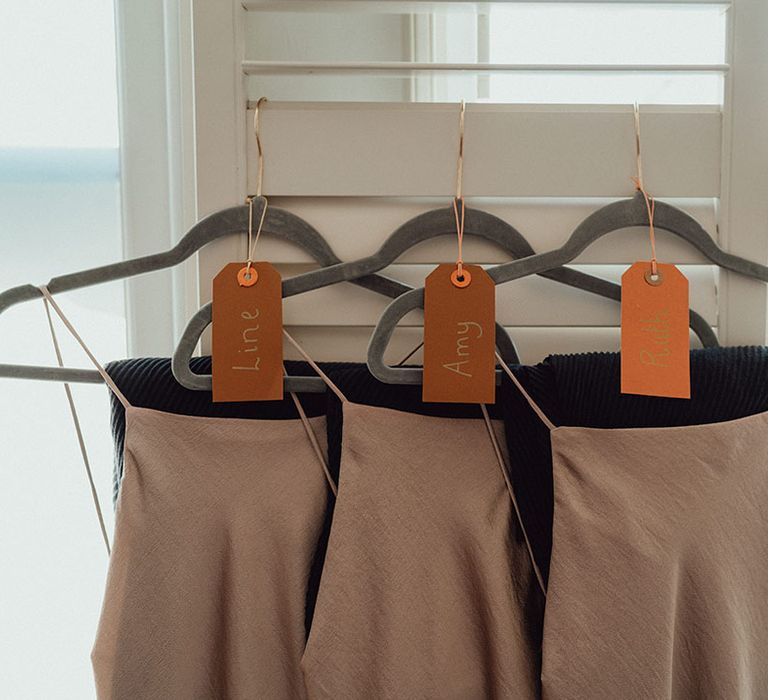 Grey velvet hangers with champagne gold bridesmaid dress and name tags on orange labels 