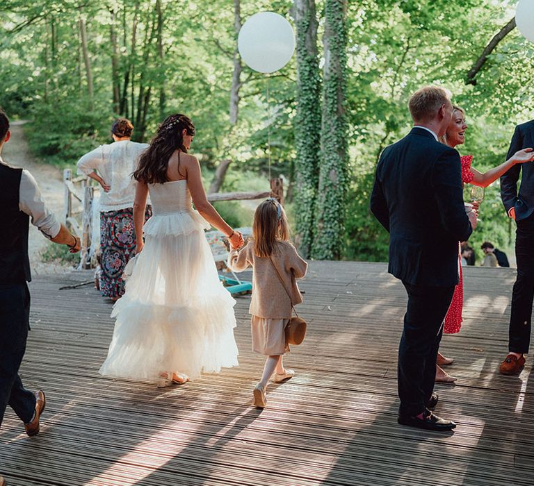 Bride in a strapless ruffle wedding gown walks holding hands with a young girl on the decking at Weald and Downland Living Museum venue 