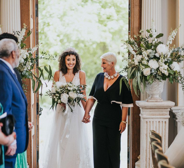 Black bride holds white floral bouquet and walks down the aisle with her mother at Orleans House Gallery