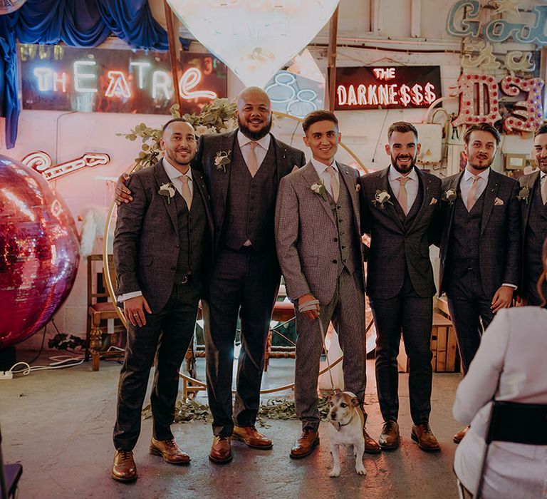 Groom in grey three piece wedding suit with yellow suit and yellow pocket square standing with groomsmen in matching dark grey three piece suits with yellow ties and boutonnieres at Gods Own Junkyard 