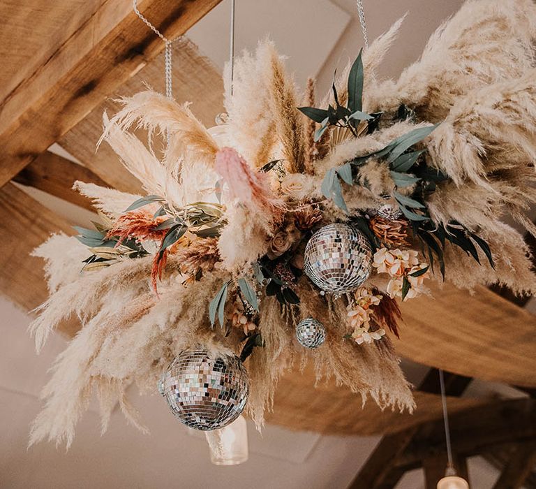 Disco balls attached to a large pampas grass flower installation with leaves 