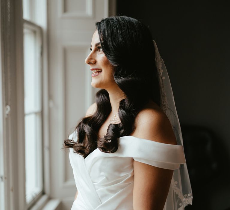 Bride wears off-the-shoulder wedding dress with sweetheart neckline and floral embellished veil 