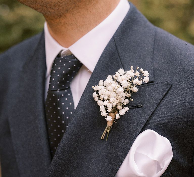 Groom in dark navy suit with matching tie with spots and white gypsophila buttonhole with white pocket square 