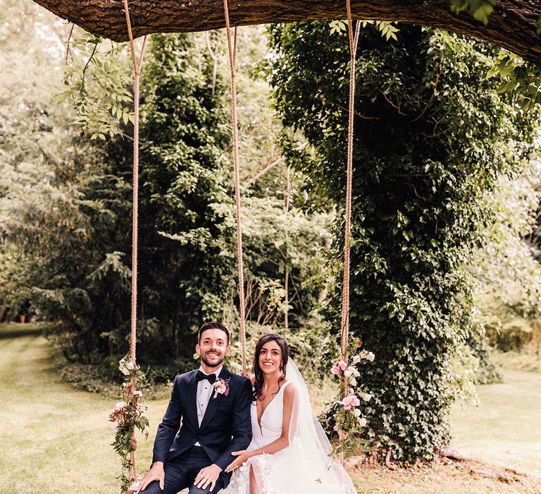 Pink rose decorated wooden wedding swing with the bride and groom seated together for their wedding portraits 