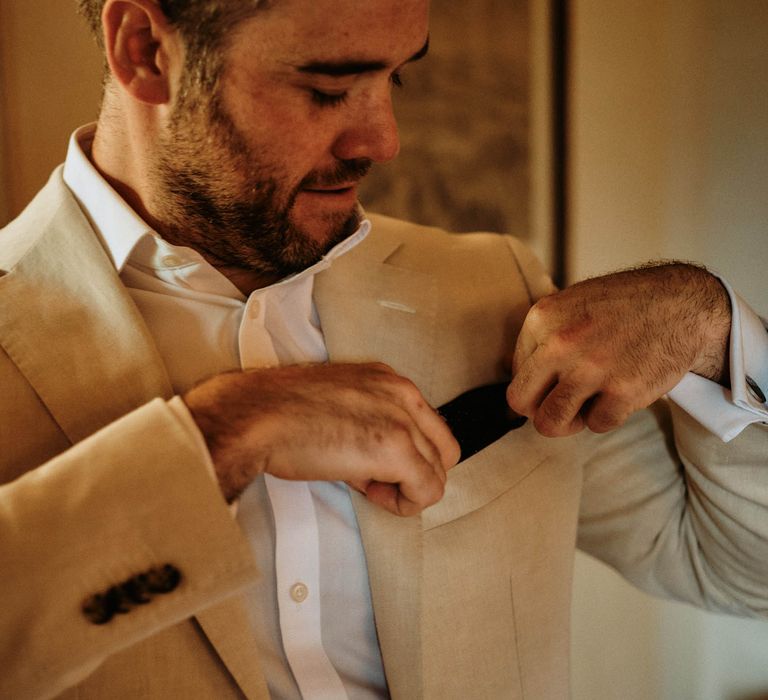 Groom checking his pocket square whilst wearing a beige linen wedding suit