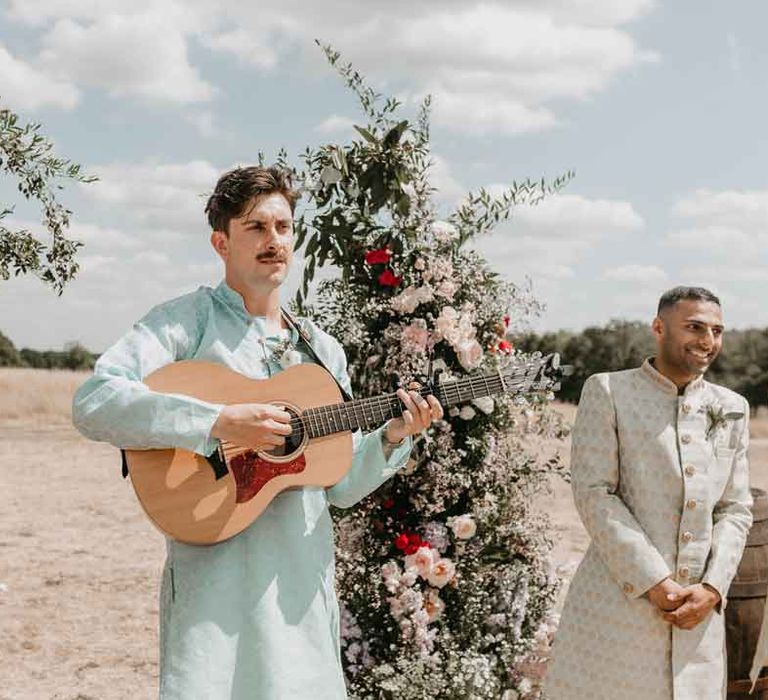 Live acoustic wedding entertainment - wedding singer in baby blue sherwani playing the guitar at Gujarati wedding ceremony standing in front of large garden rose, baby's-breath, eucalyptus, peony and foliage floral columns