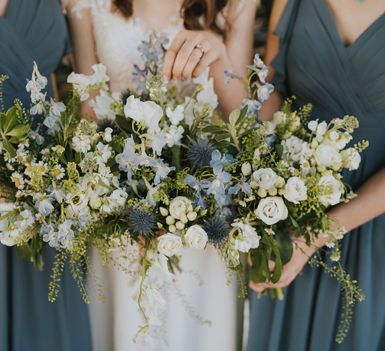 The bride and bridesmaids hold matching blue and white wedding bouquets with daisies for the rustic theme wedding at Badgers Holt 