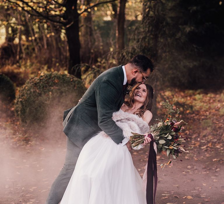 Bride in off the shoulder long balloon sleeve wedding dress with faux fur shawl kissing the groom for epic wedding photo 