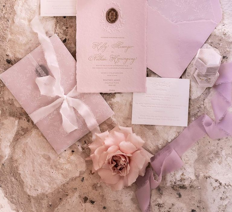 Dainty light purple and lilac wedding stationery with lilac ribbon and blush garden roses on stone floor 