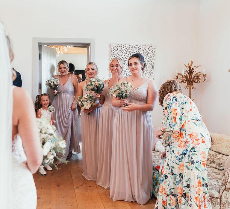 The bridesmaids in dusky pink bridesmaid dresses getting their first look at the bride in her lace wedding dress