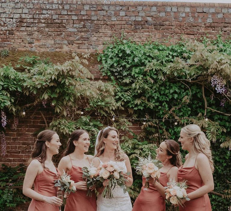 Bridal party in coral midi bridesmaid dresses with the bride at a classic wedding 