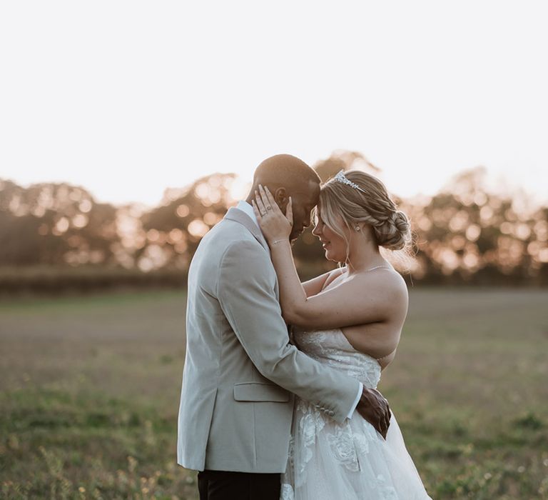 The bride in a floral lace wedding dress with pearl tiara embraces groom in velvet black tie suit 