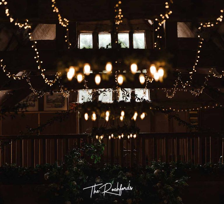 Lains Barn wedding venue with fairy lights, suspended foliage arrangements, festoon chandeliers, large neon wedding sign, foliage wall and candles 