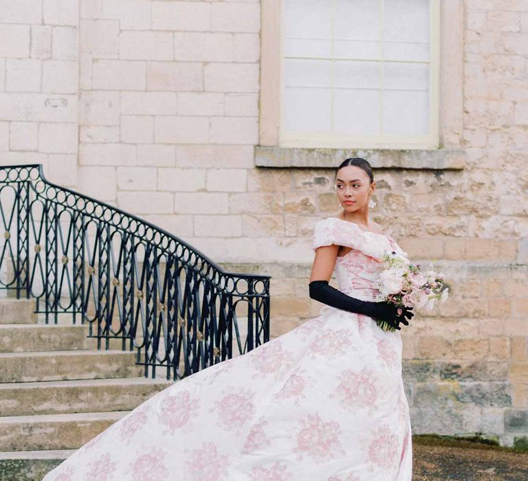 Bride in off the shoulder white and pink floral patterned bridal gown with black bow and front slit and long black satin gloves at Settrington Orangery