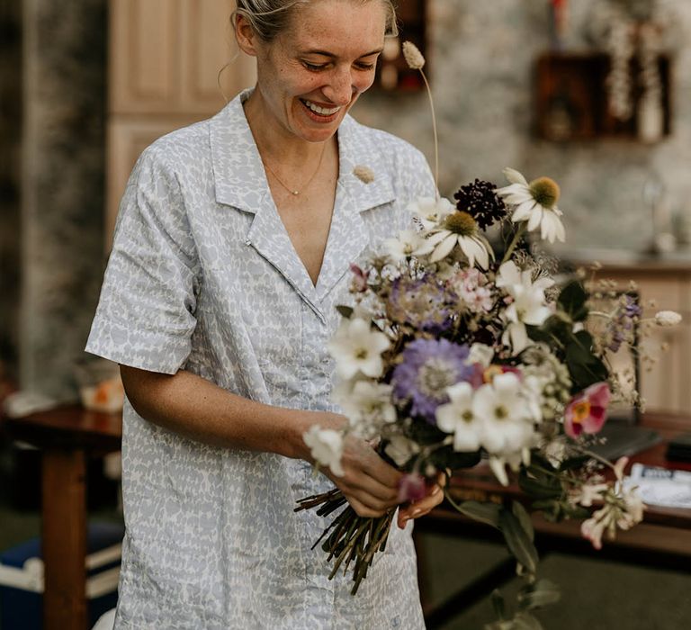 Bride in blue and white patterned wedding pyjamas holding her bridal bouquet with British wildflowers 