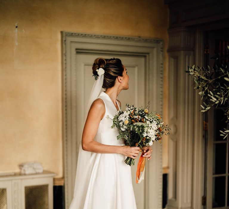 Bride in traditional sleeveless wedding dress with bun hairstyle with white flower hair accessory and veil 