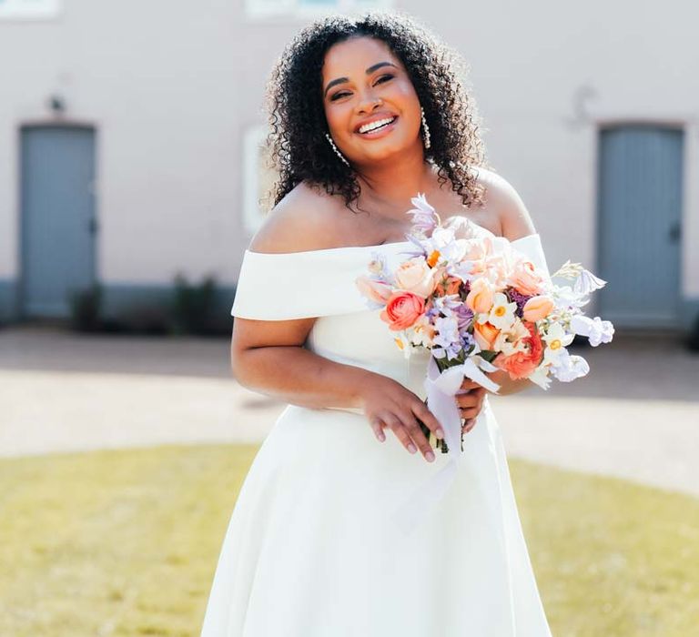 Bride in off the shoulder wedding dress with puddle train holding orange, lilac and peach mixed flower bridal bouquet at Rackleys Barn