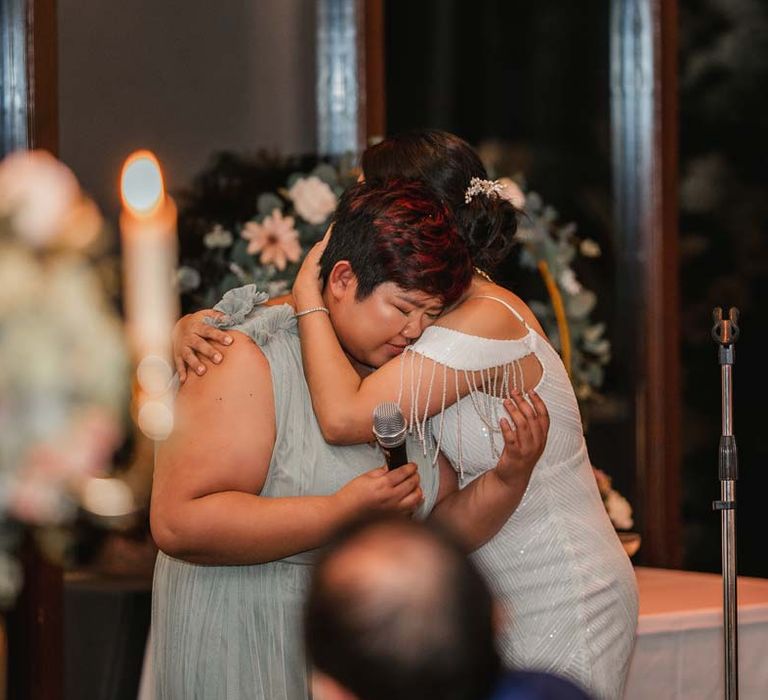 Bride in white beaded and sequined slip wedding dress hugging wedding guest during heartfelt wedding speeches