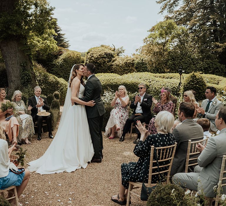 The bride and groom share their first kiss as a married couple as their wedding guests watch in a circle 