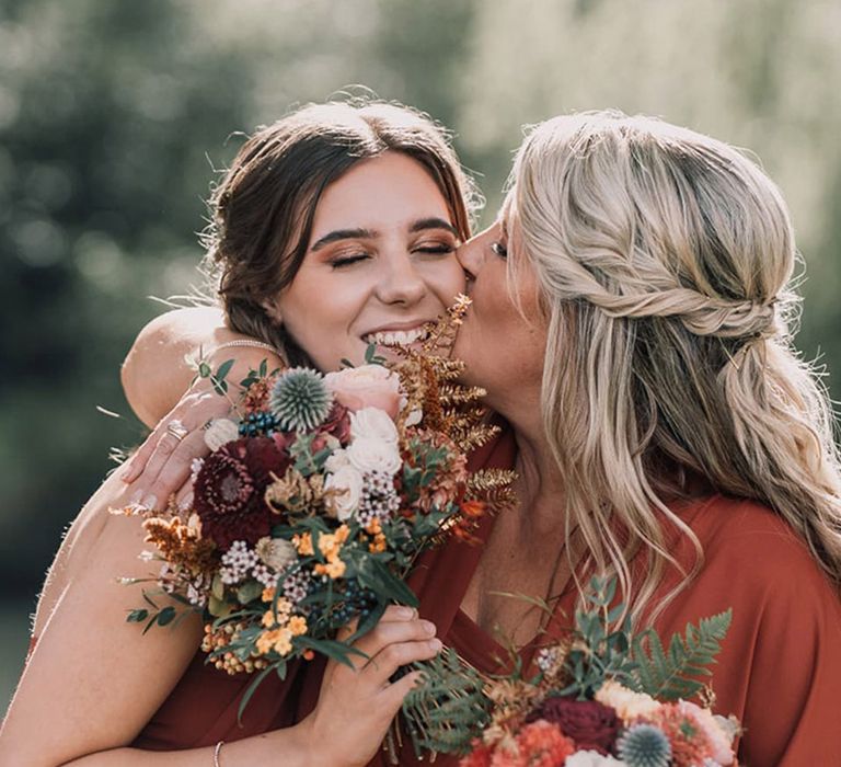 Bridesmaids in orange bridesmaid dresses wearing red and white roses with thistles 