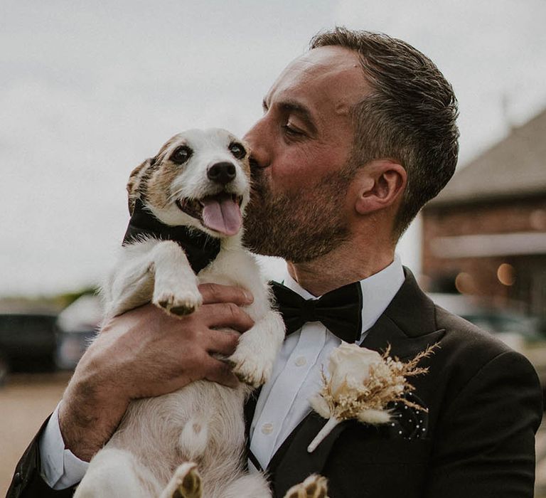 Groom holds the pet dog wearing a black bow tie for the wedding 