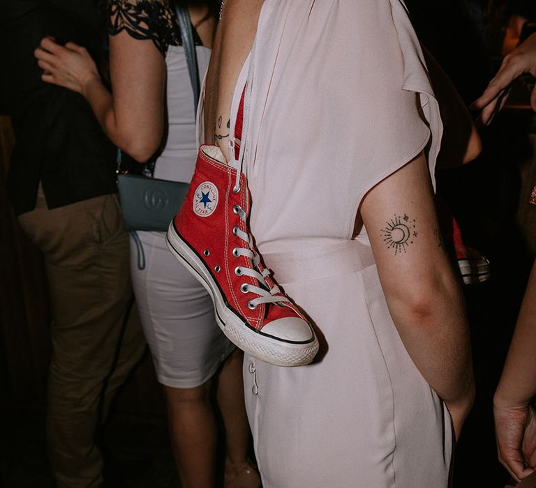 A wedding guest dances on the dance floor with red Converses draped around her 