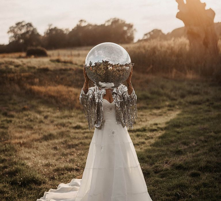 Bride wearing sparkly tassel wedding jacket holding giant disco ball 