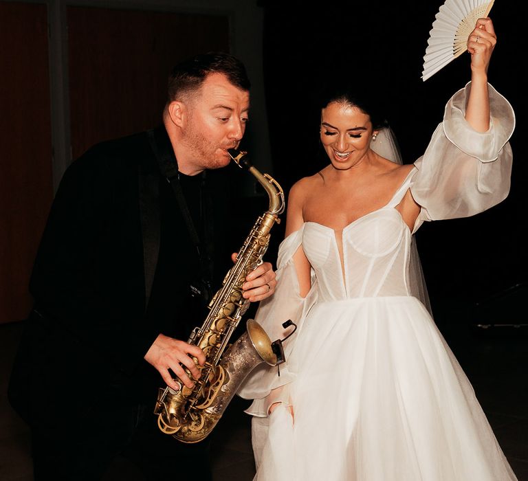 Bride in white tulle wedding dress dances with fan next to saxophonist at Crumplebury wedding