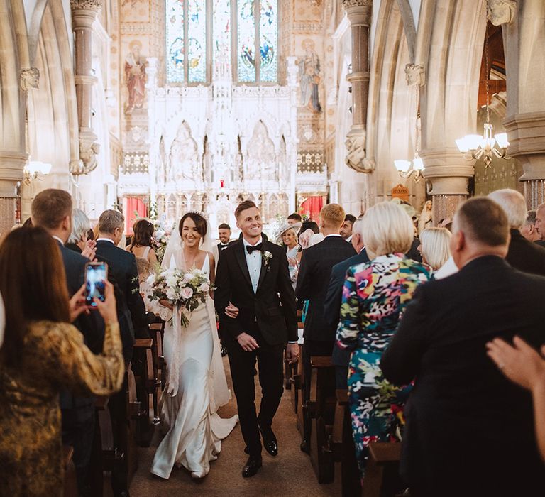 The bride and groom walk back down the aisle at their church wedding 