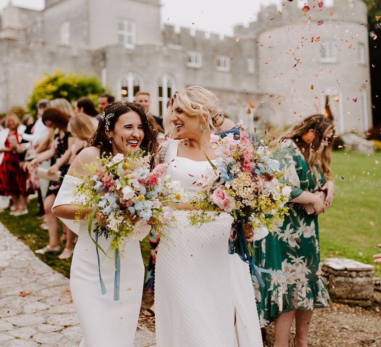 Two brides walking with pastel pink and blue wedding bouquets at castle wedding venue 