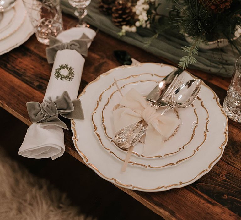 Festive christmas winter wedding place setting with white plates, silver cutlery tied with white bow and wedding crackers decorated with velvet bows 