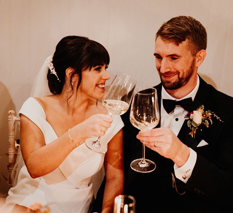 The bride and groom cheers their glasses together in a toast at the wedding 