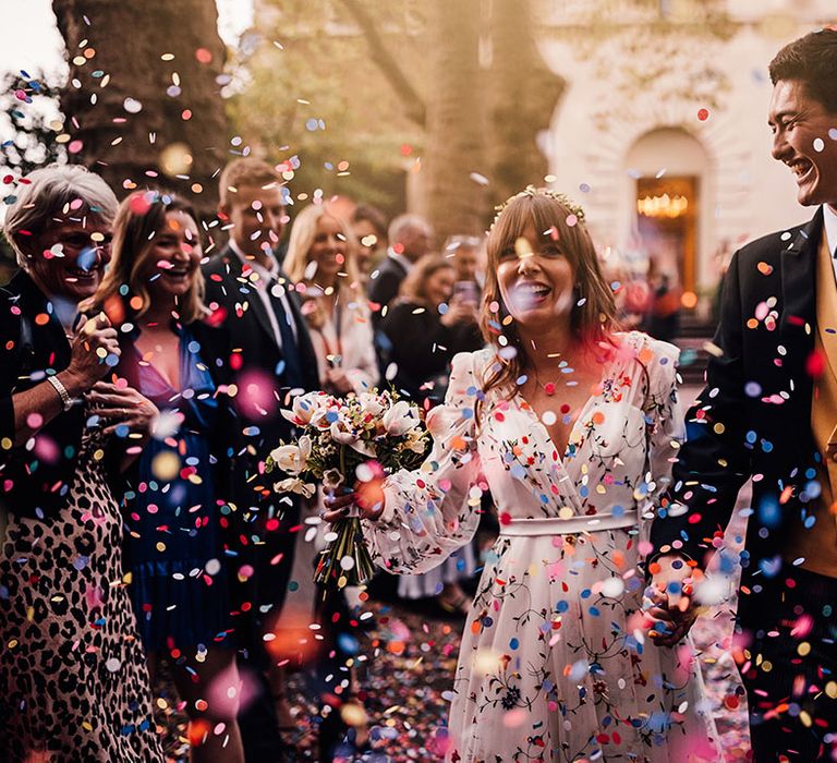 Romantic wedding confetti moment with the bride and groom smiling with joy as guests throw confetti over them 