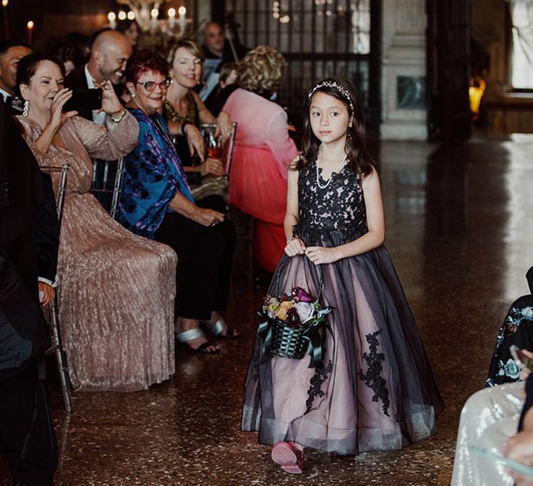 Flower girl in black dress at gothic ornate wedding walking down the aisle 