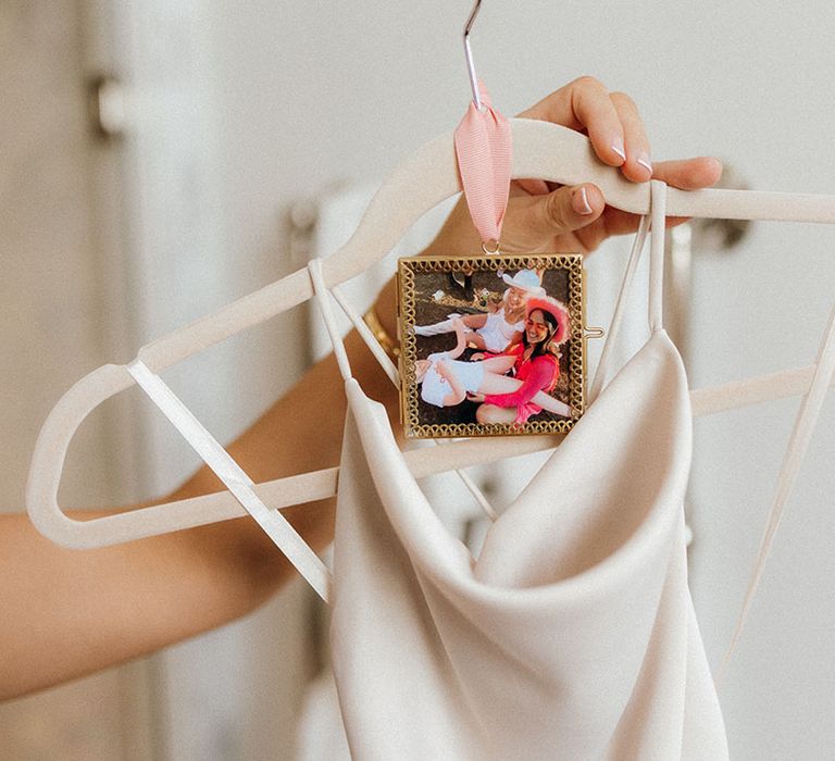 Photos of the bride and the bridesmaid attached to the hanger holding the bridesmaid's dress 