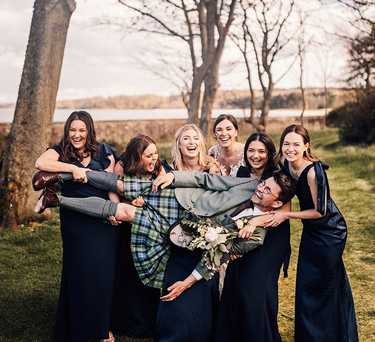 bridal-party-wearing-navy-blue-bridesmaid-dresses-carrying-groom-in-kilt