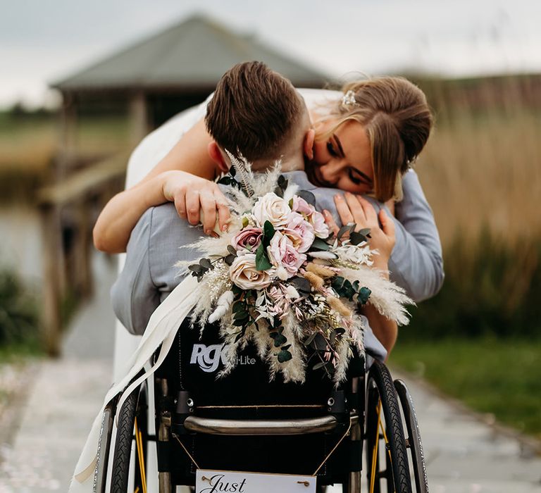 just-married-wedding-sign-on-wheelchair-with-bride-embracing-groom-holding-pampas-bouquet