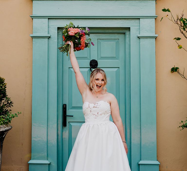 bride-in-floral-strapless-wedding-dress-with-bouquet-in-front-of-blue-door