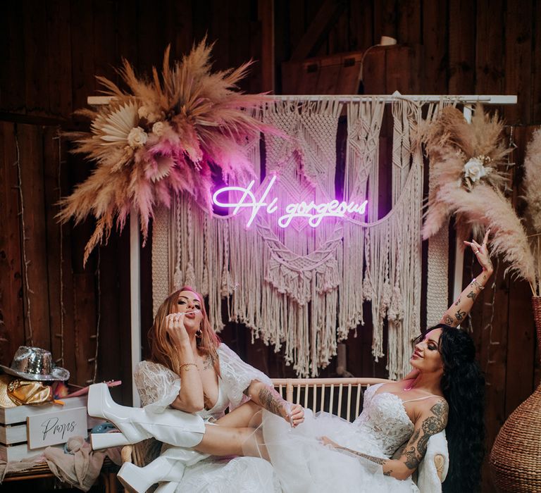 neon-sign-pampas-grass-and-macrame-backdrop-with-two-brides-posing-together