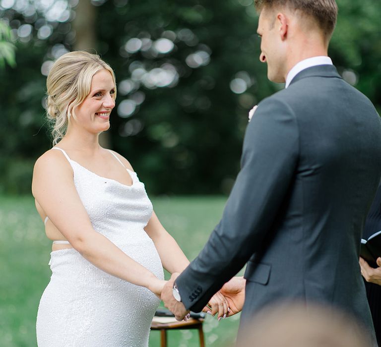 bride-in-beaded-maternity-wedding-dress-holding-hands-with-groom-at-outdoor-wedding