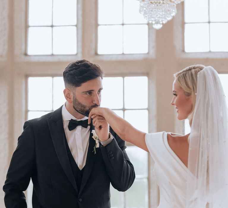 groom-in-black-tuxedo-kissing-bride's-hand