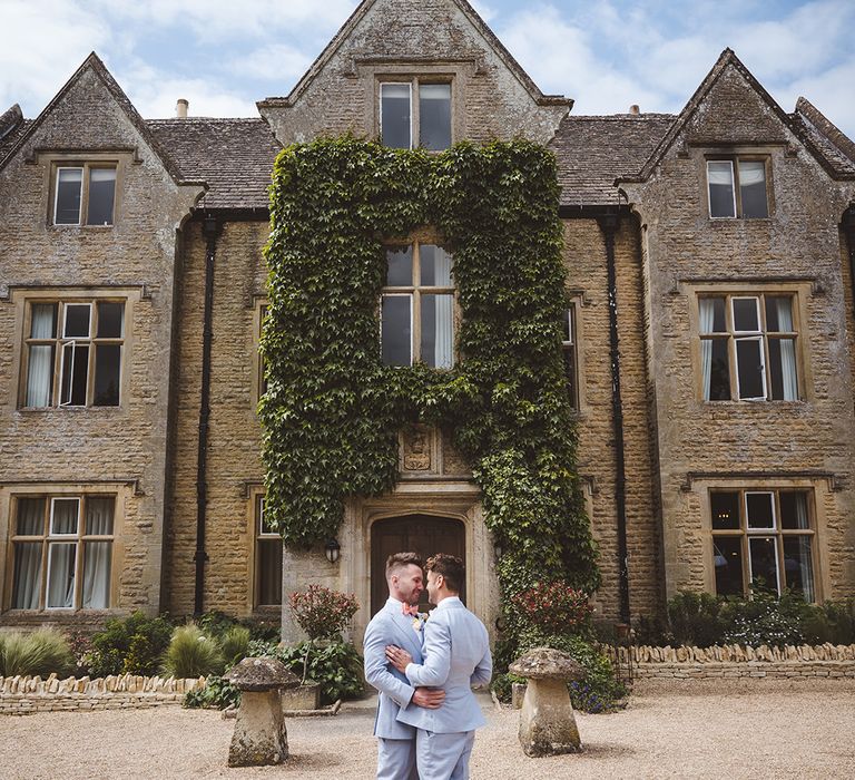 two-grooms-in-light-blue-suits-kiss-at-country-house-wedding-venue