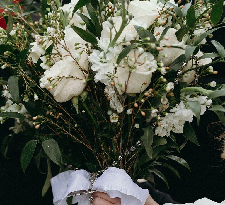 bride-holding-white-rose-bouquet-with-white-ribbon-and-cross-charm